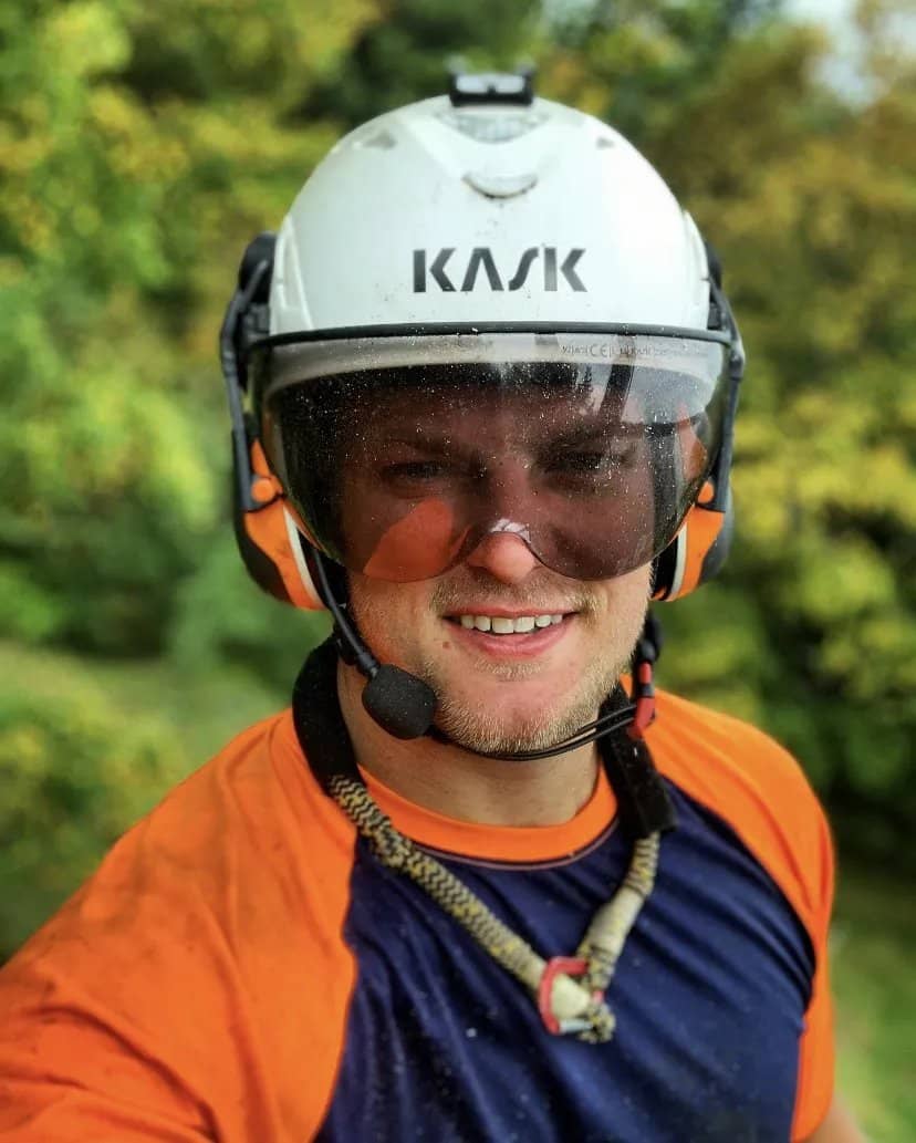Arborist in an orange shirt wearing a helmet and face shield.
