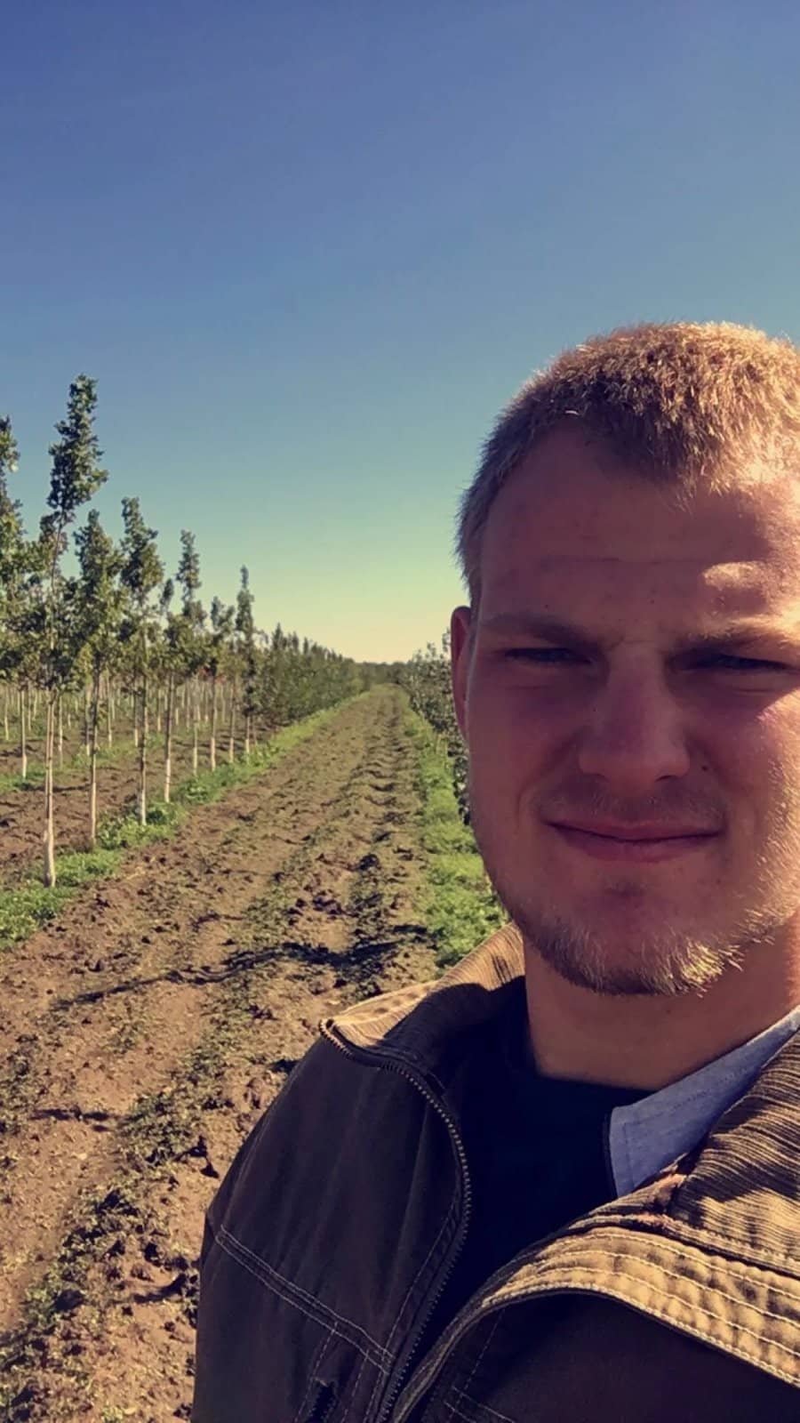 Portrait beside rows of young trees in a field.