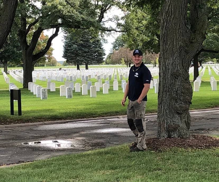 Arborist beside a tree near rows of white cemetery headstones.