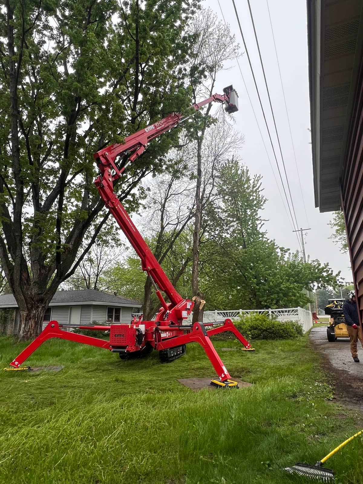 Red tracked lift extended beside a house and overhead wires.