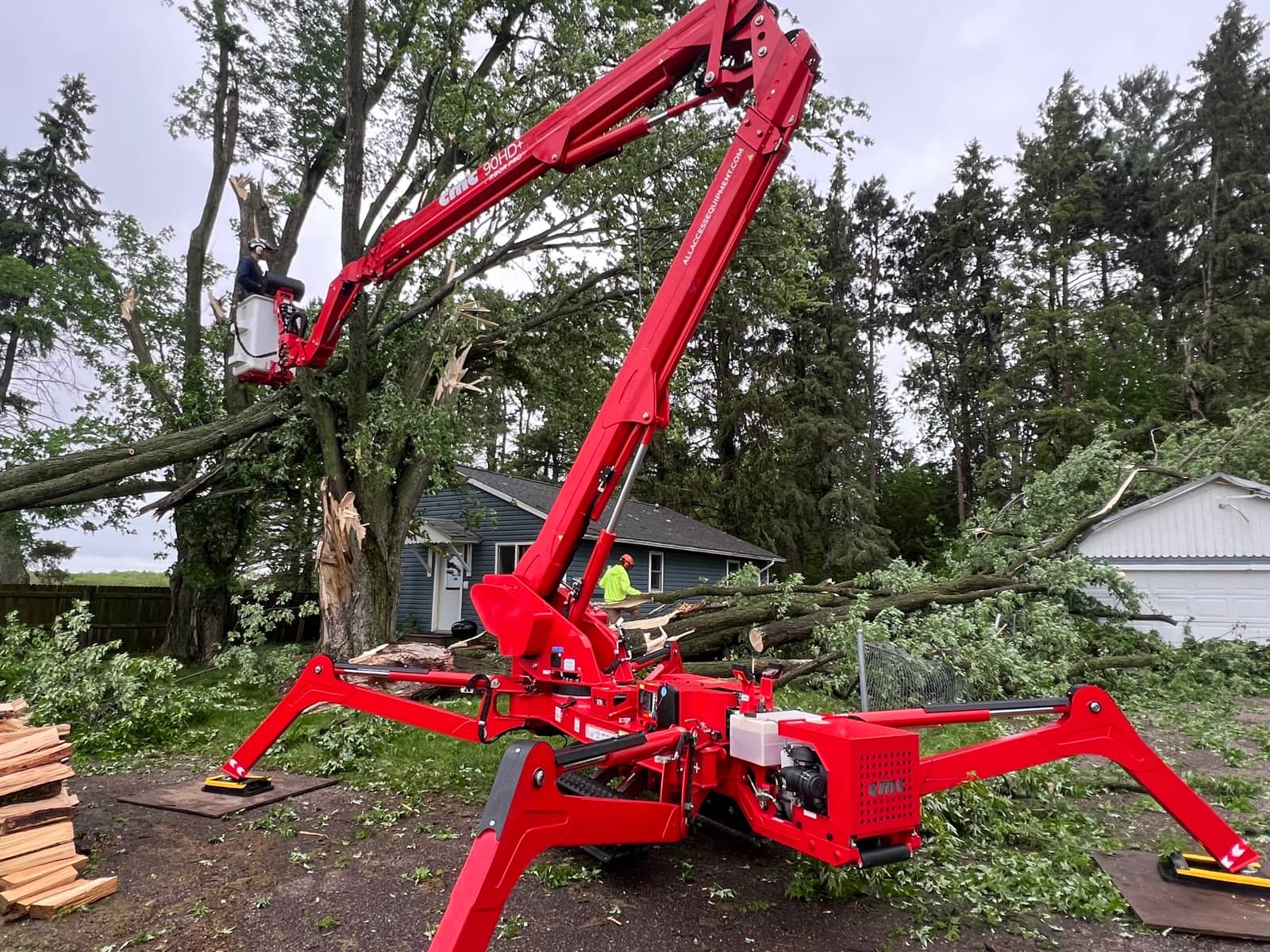 Arborist in a red lift beside a split tree and fallen branches.