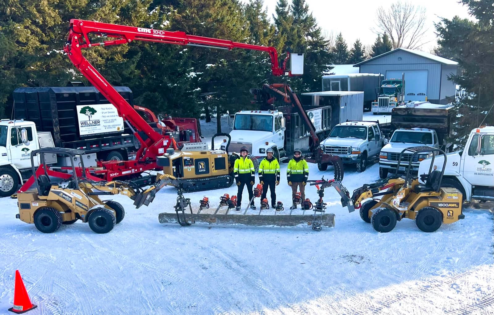 Tree care crew with trucks, lifts, loaders, and tools in a snowy yard.